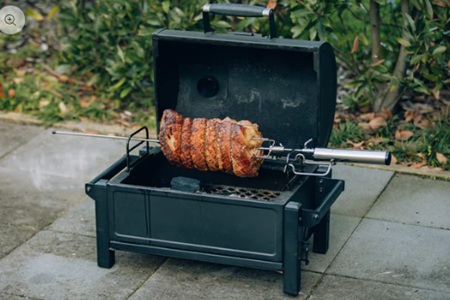 Rotisserie BBQ cooking — spit-roasted meat seasoned with black pepper rub and spices over open fire